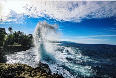 Waves splashing on rocks against sky