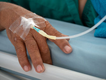 Close-up of human hand with iv drip on bed