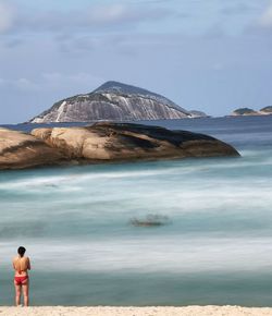 Rear view of woman standing on sea shore against sky