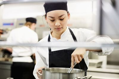 Young female chef stirring pot in kitchen at restaurant