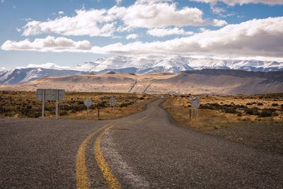 Empty road leading towards mountains against sky