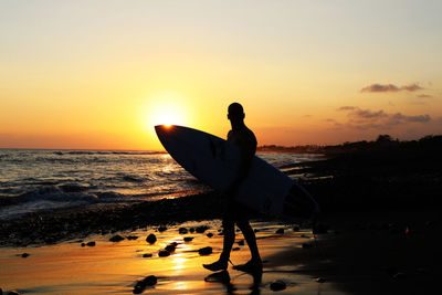 Silhouette man with surfboard on beach against sky during sunset