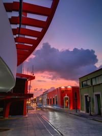 Road amidst buildings against sky at sunset