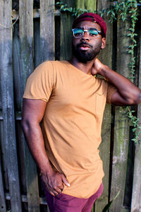 Young man wearing sunglasses standing against fence