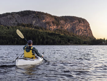 Man paddles in kayak across moosehead lake towards mount kineo, maine