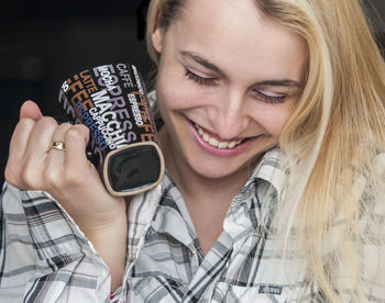 Happy young woman holding coffee cup against black background