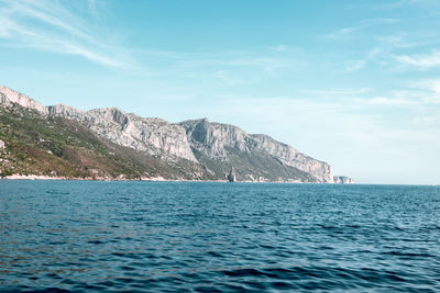 Scenic view of sea by mountain against sky