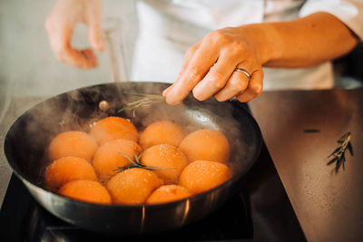 Hand of a chef adding rosemary to the cooking in a frying pan apricots