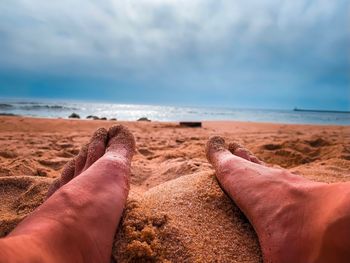 Low section of man on sand at beach against sky