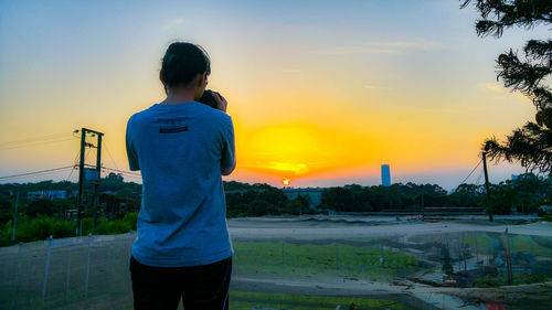 Rear view of boy standing against sky during sunset