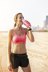 Female athlete drinking water while standing at beach