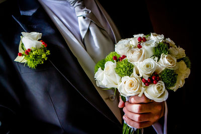 Midsection of groom holding flower bouquet