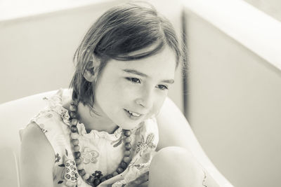 Smiling girl looking away while sitting against wall