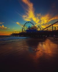 Amusement park at beach against sky during sunset