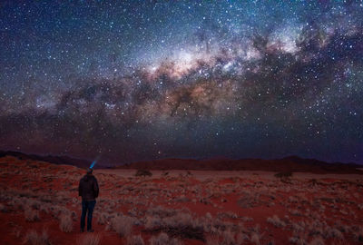 Rear view of man standing in the desert against sky at night