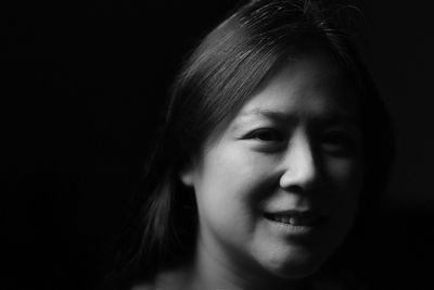 Close-up portrait of smiling woman against black background