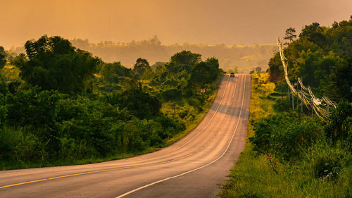 Road amidst trees against sky during sunset