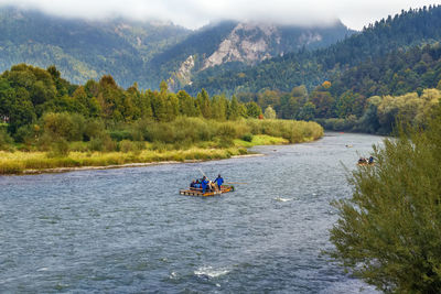 People on boat in river against mountains