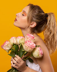 Side view of woman with pink roses against yellow background