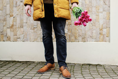 Blond man in a yellow winter jacket with a bouquet of tulips in hands