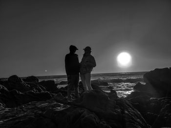 Man and lady standing on rock at beach against sky