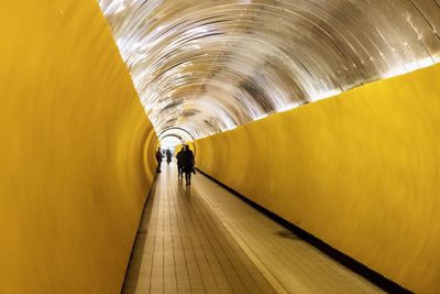 Rear view of people walking in illuminated tunnel