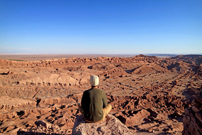Hiker sitting on rocky cliff admiring the moon valley or valle de la luna in atacama desert of chile