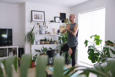 Man with hands clasped practicing tree pose in living room at home
