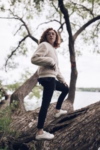 Portrait of smiling young woman against tree trunk