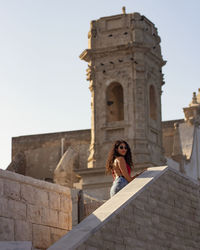 Woman standing on staircase of historic building against clear sky