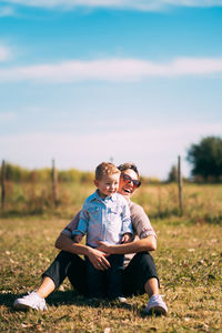 Woman with son sitting on field on sunny day