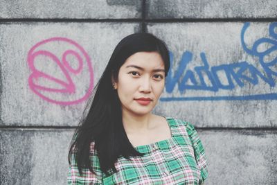 Portrait of young woman standing against graffiti wall