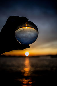 Close-up of hand holding sea against sky during sunset