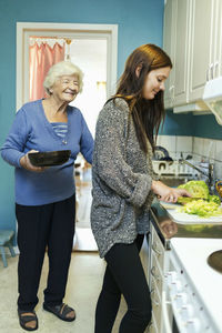 Happy elderly woman with granddaughter preparing food in kitchen at home