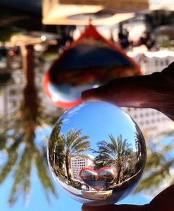 Close-up of hand holding crystal ball with reflection of trees