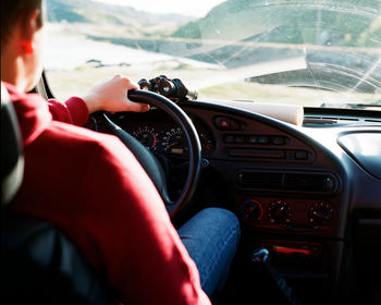 A man sits at the wheel of a car with a map and binoculars