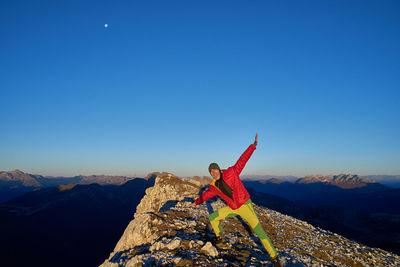 Man on rock in mountains against blue sky