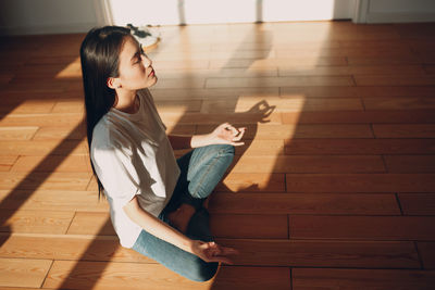 Young woman looking away while sitting on floor at home