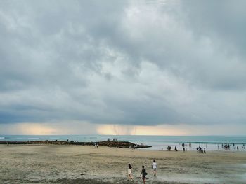 People at beach against cloudy sky