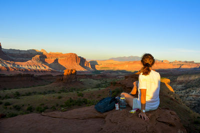 Man sitting on rock looking at mountain against clear sky