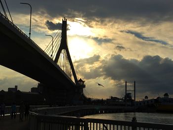 Silhouette bridge over river against cloudy sky