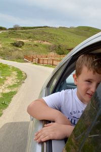 Rear view of boy on car by road