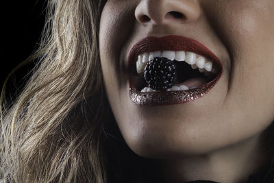 Closeup of blonde woman smiling with healthy teeth, red lipstick and biting a raspberry.