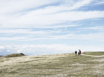 Rear view of friends walking on mountain peak against cloudy sky