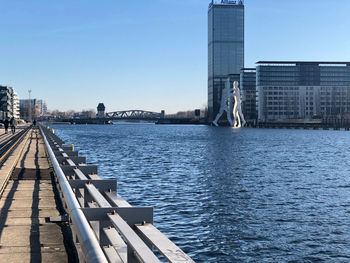 Bridge over river by buildings against clear blue sky