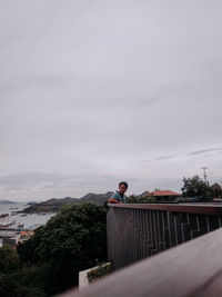 Man standing by railing against sky