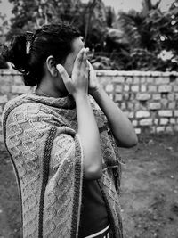 Woman with hands covering eyes standing on land against trees