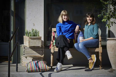 Full length portrait of smiling owners sitting on bench outside store