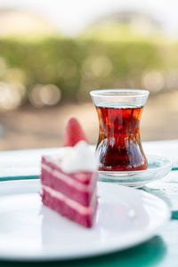 Piece of red velvet cake decorated with fresh berries in a white plate on the table, a cup of