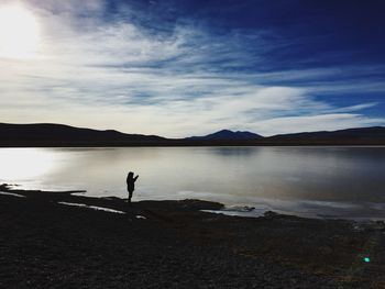 Silhouette person standing by lake against sky